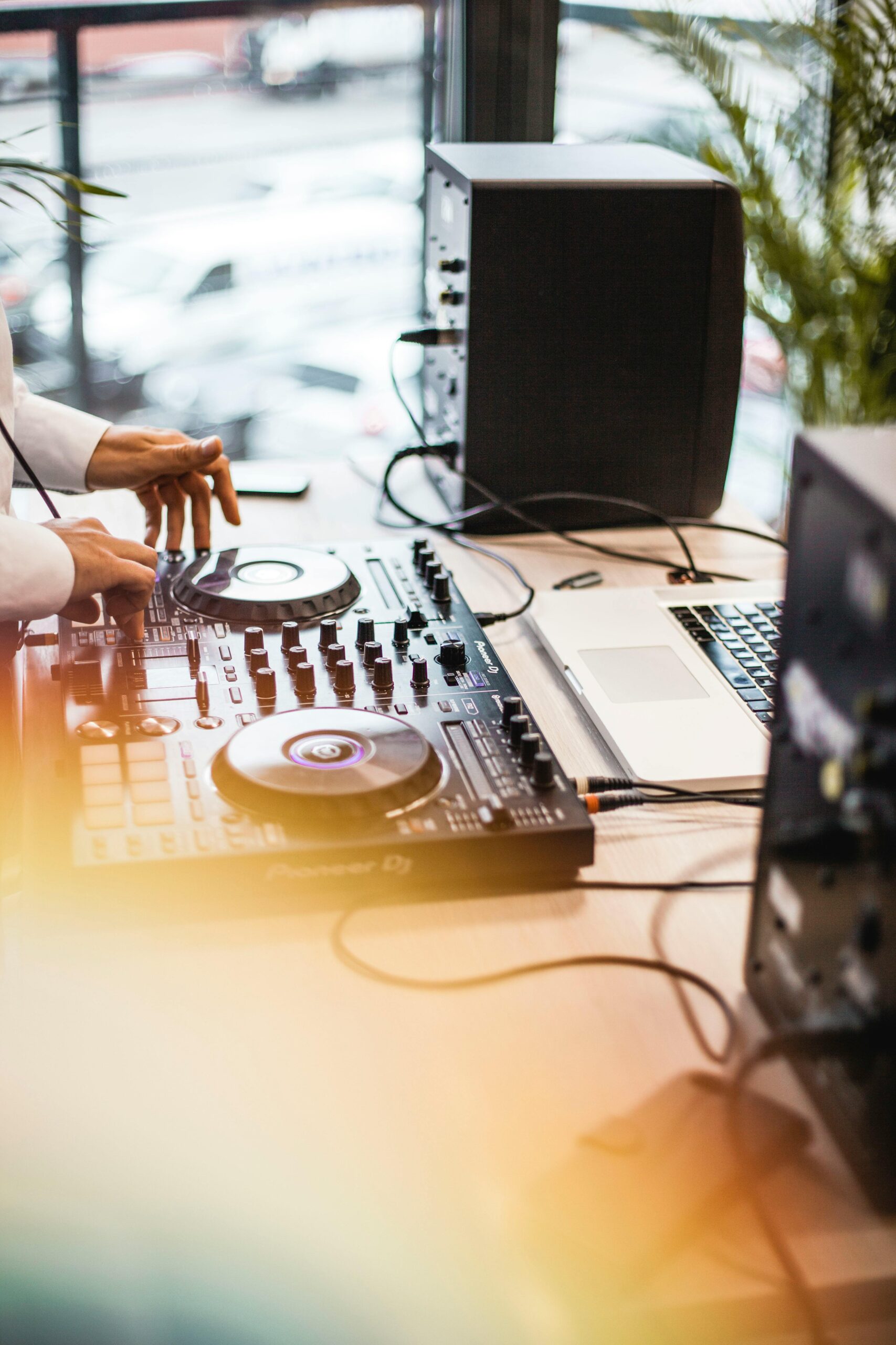 A DJ uses a mixing panel and laptop indoors, blending music tracks seamlessly.