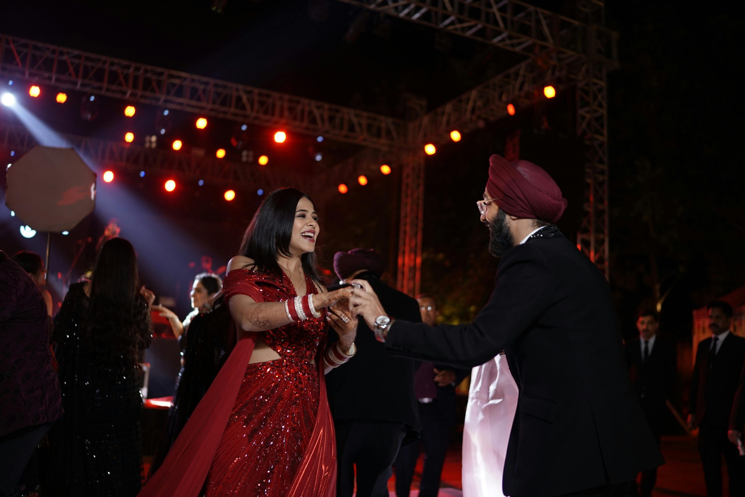 A lively moment at an Indian wedding with a couple dancing energetically amidst guests under glowing lights.